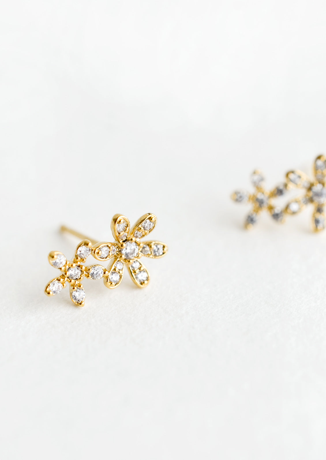A pair of gold stud earrings in a two flower silhouette with clear crystal detailing.