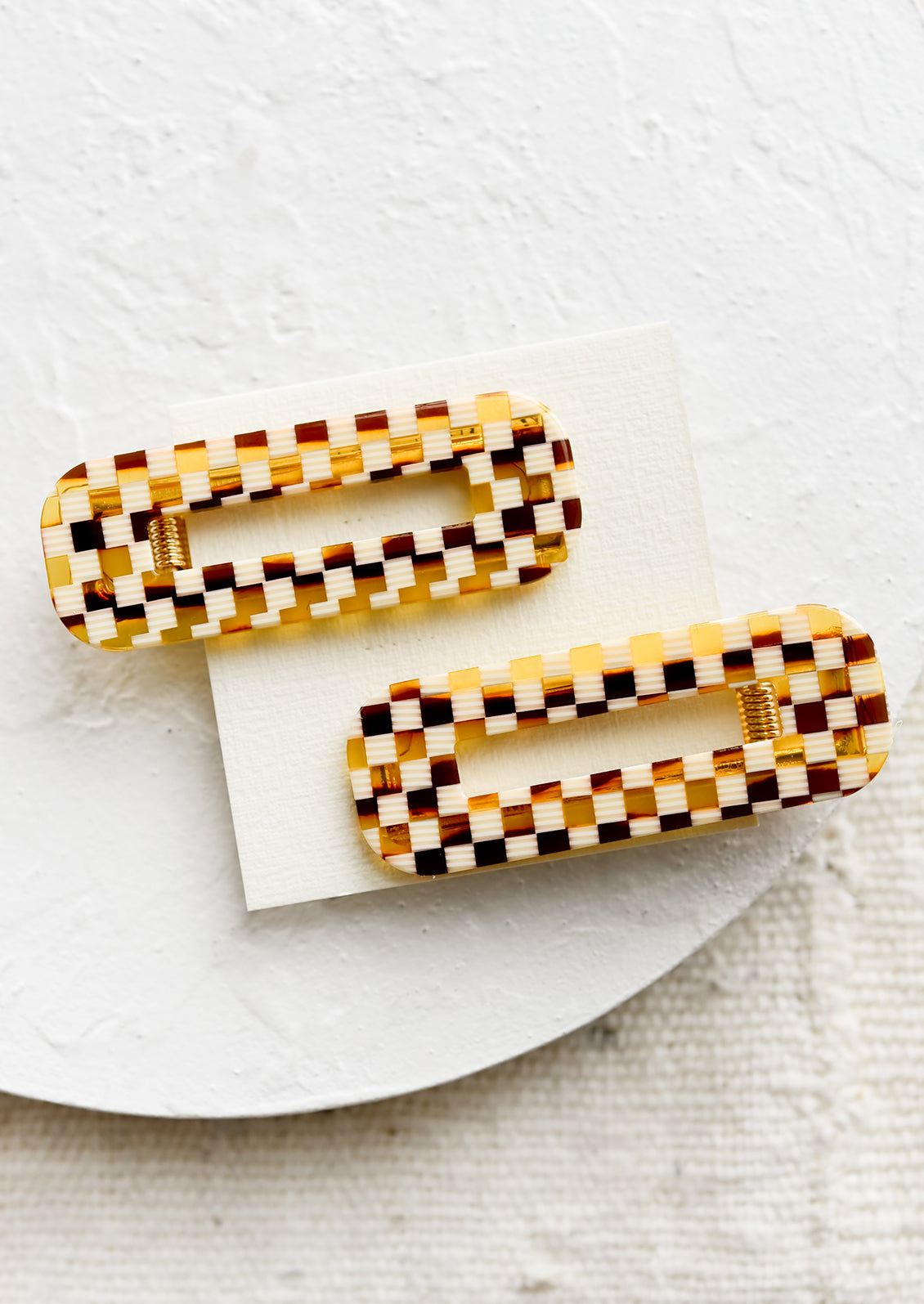 A pair of open rectangle shaped acetate hair clips in brown basketweave checker print.