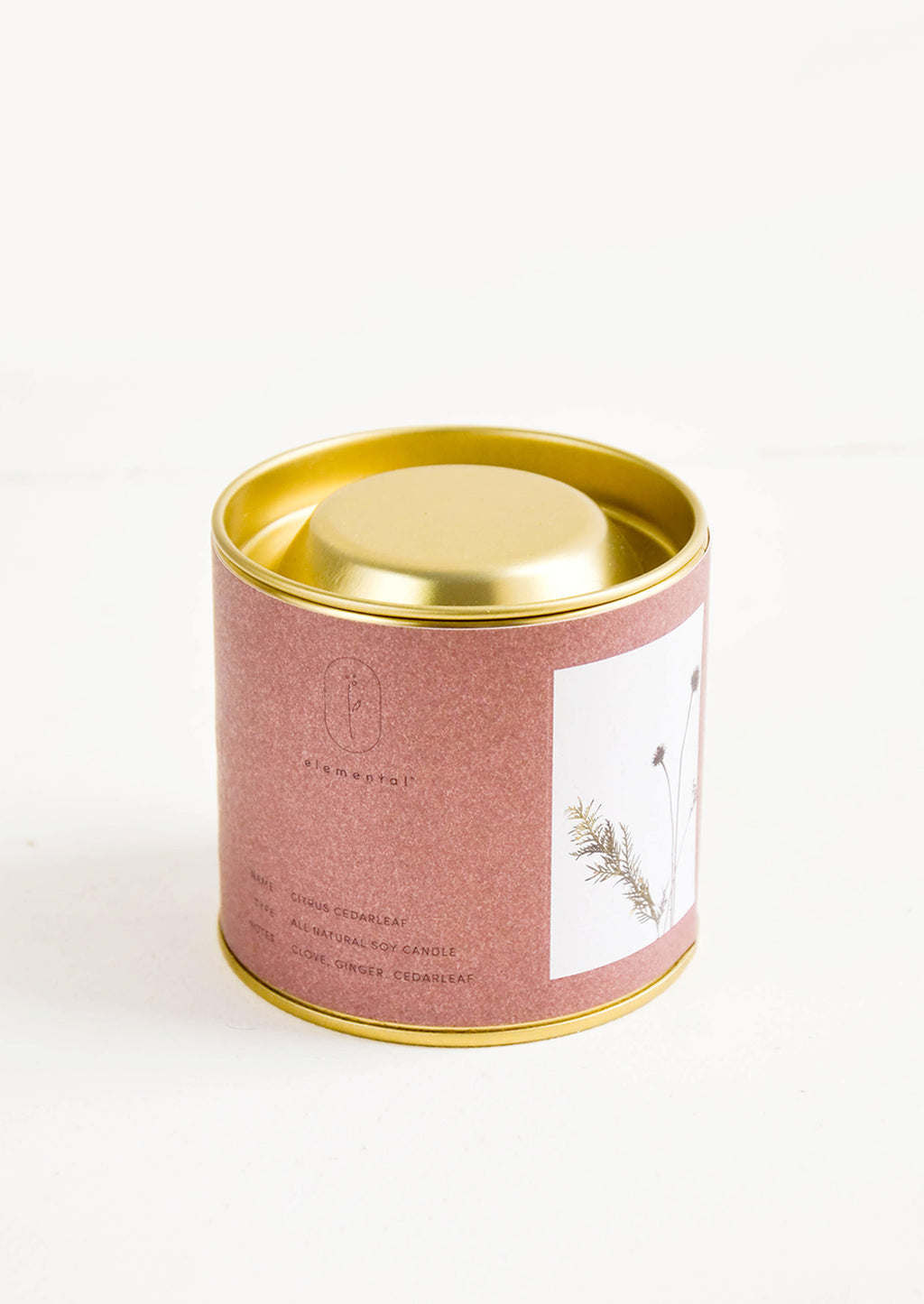 Citrus Cedarleaf: A candle in a brass tin with a dark red label featuring a picture of a flower.