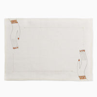 2: A white linen placemat with hemstitch border and embroidered hands at two corners.