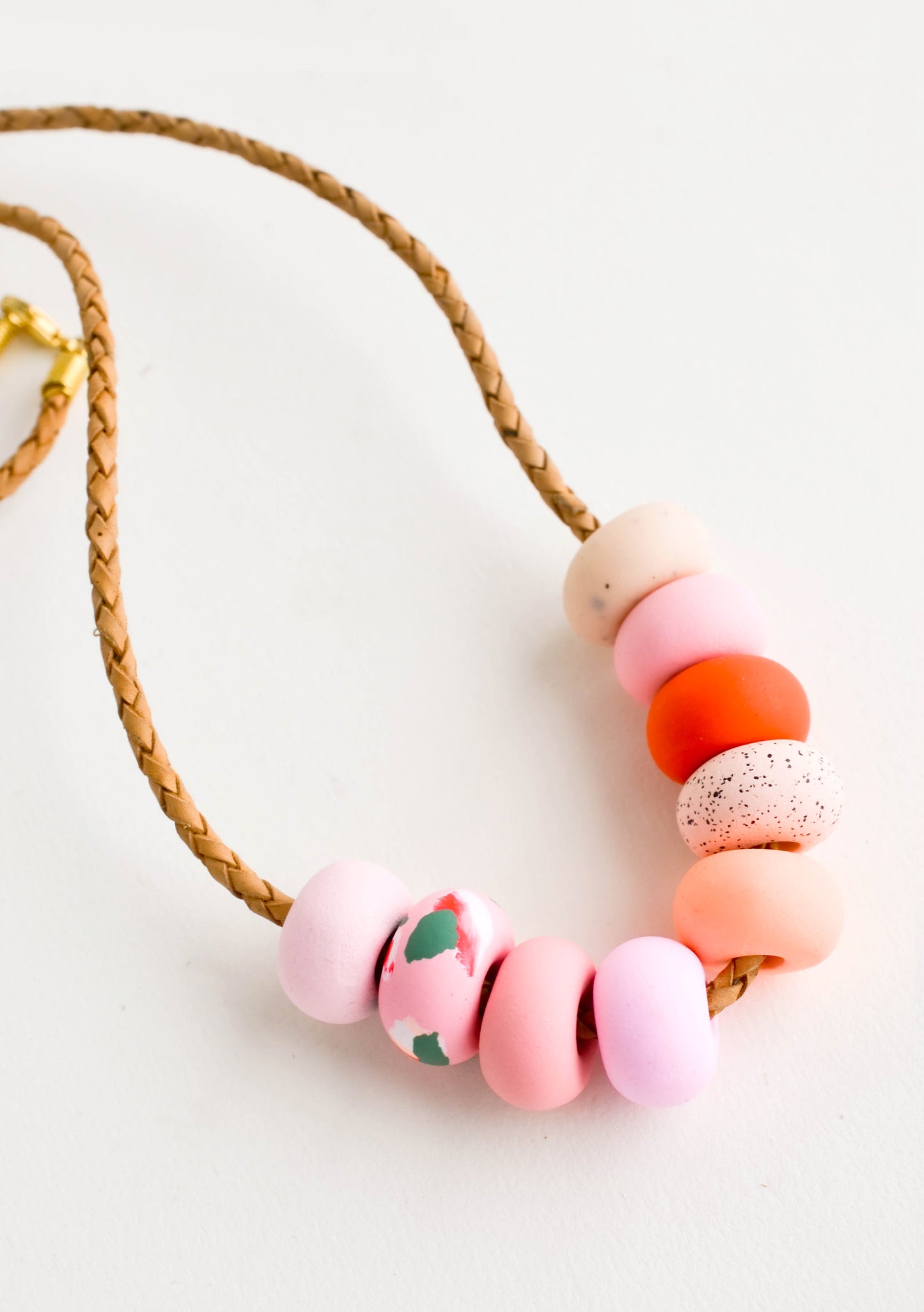 Round clay beads in pink, peach and red hues on leather cord