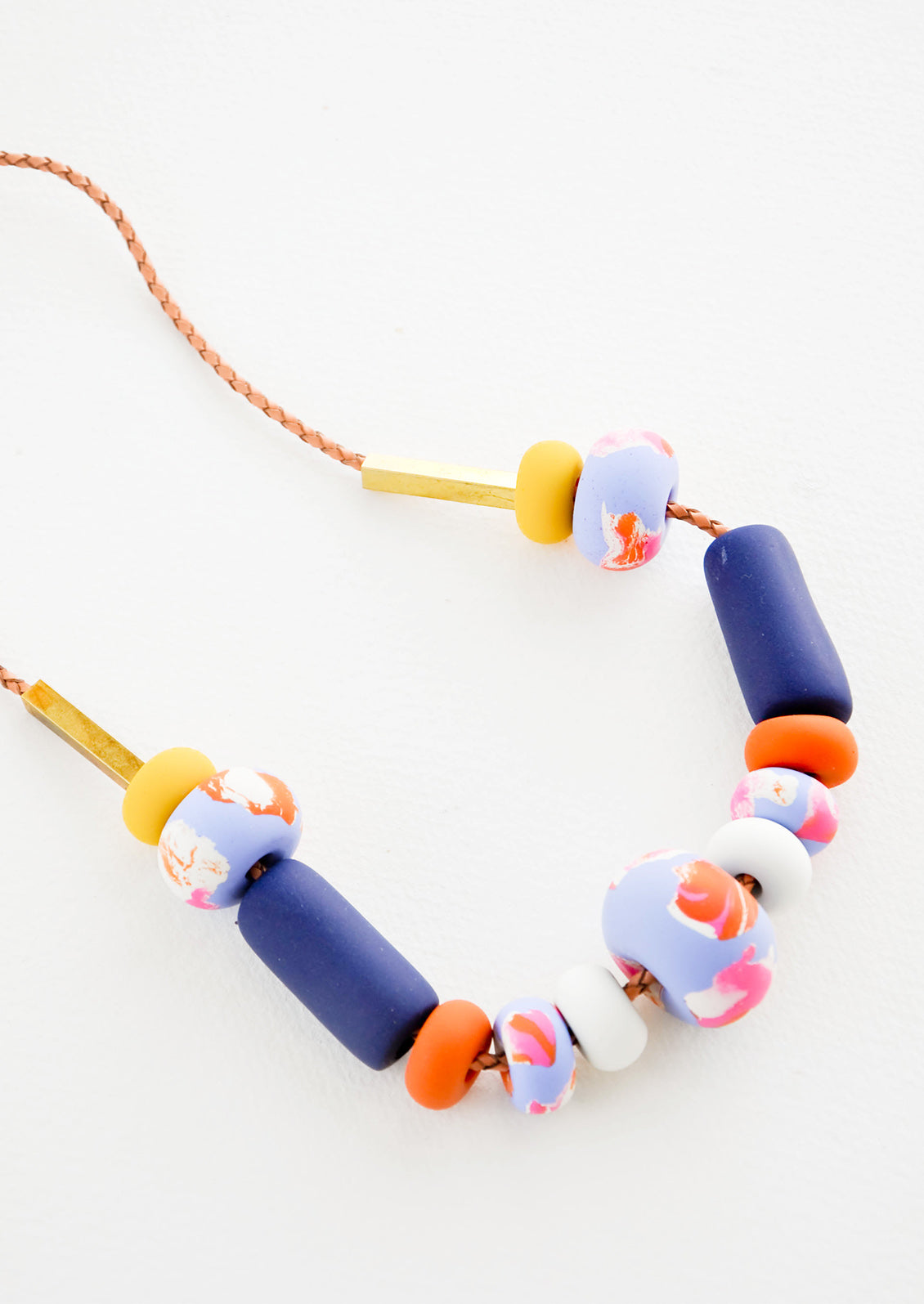 Close-up of necklace showing square off brass beads, multi-colored clay beads, and leather cord.
