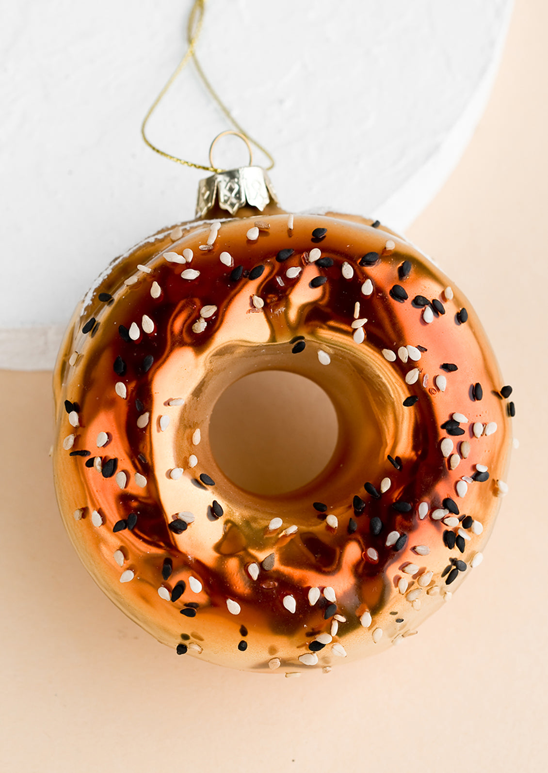 A glass ornament of a bagel with sesame seeds.