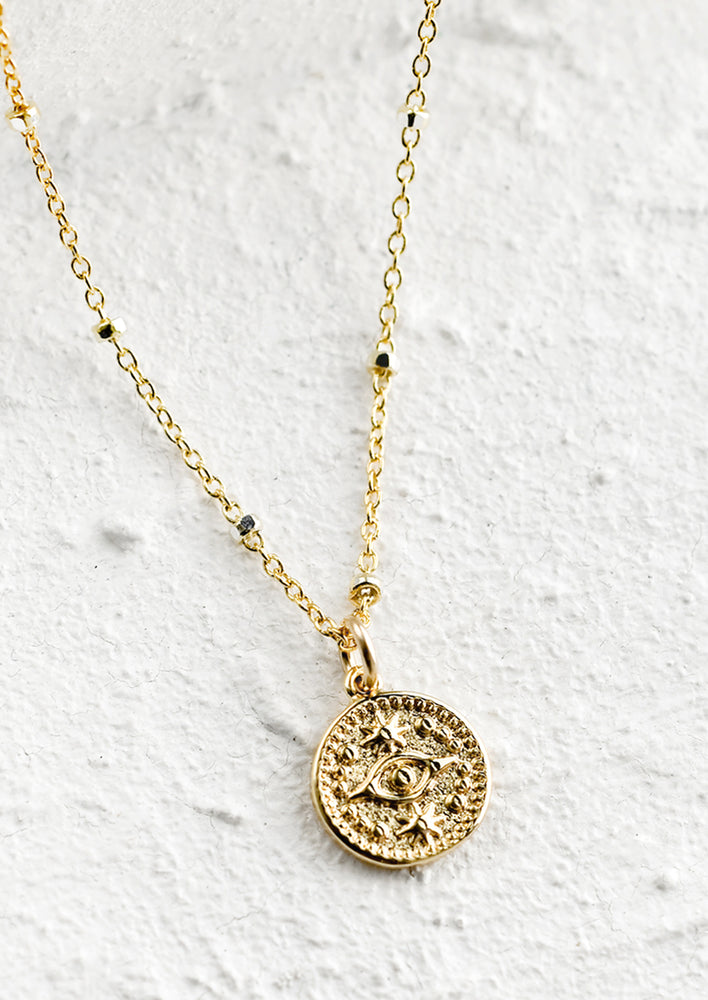 1: A gold necklace with round evil eye charm.