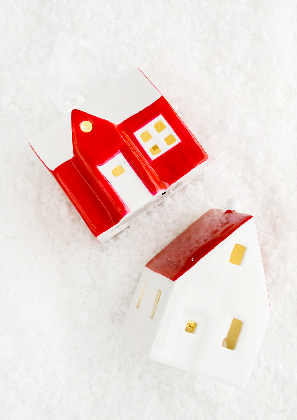 A ceramic christmas ornament in the shape of a farmhouse painted in red and white with interior lights.
