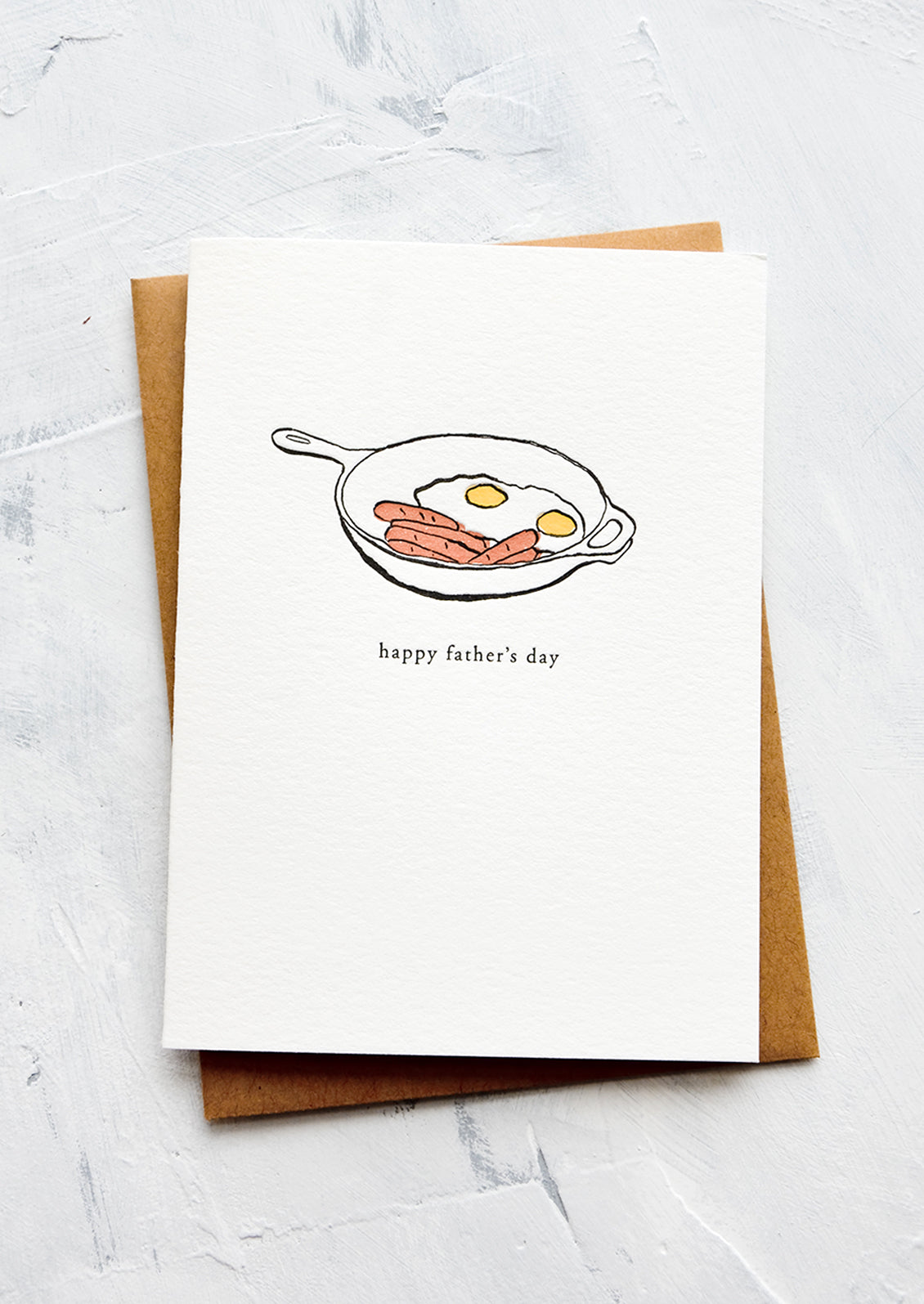 A letterpress printed greeting card with an image of cast iron skillet with eggs and bacon. Text below image reads "happy father's day".