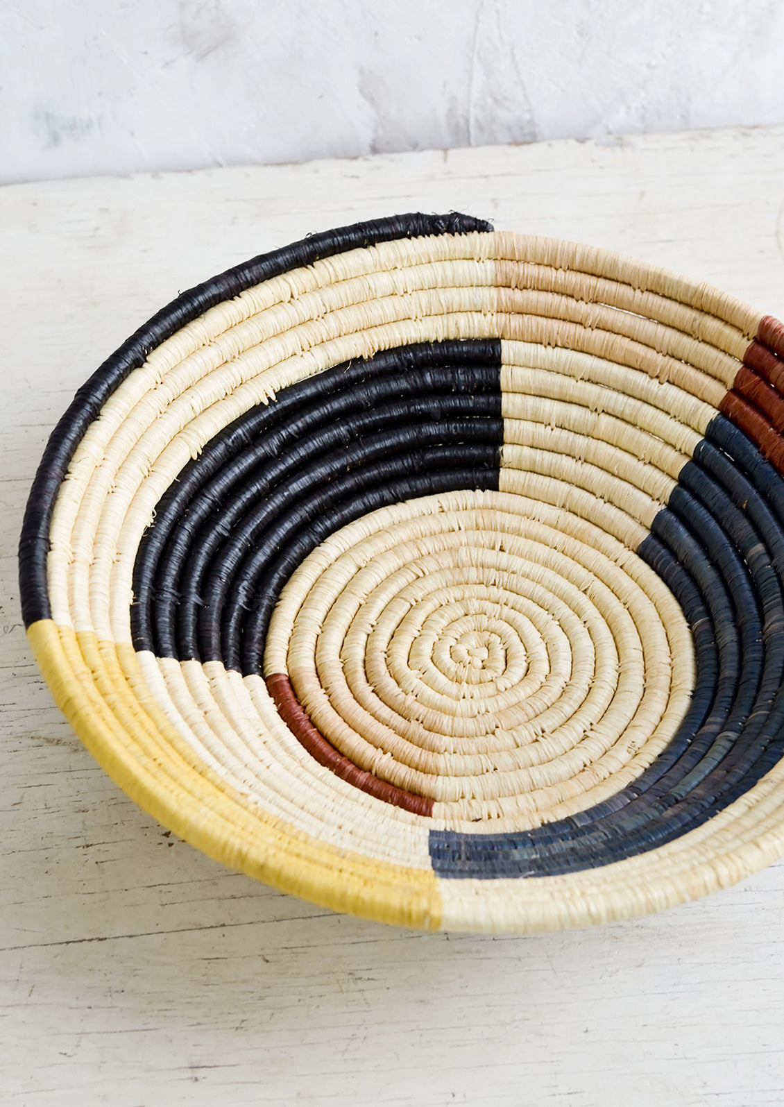 A round bowl made of raffia with a color blocked design in muted primary hues.