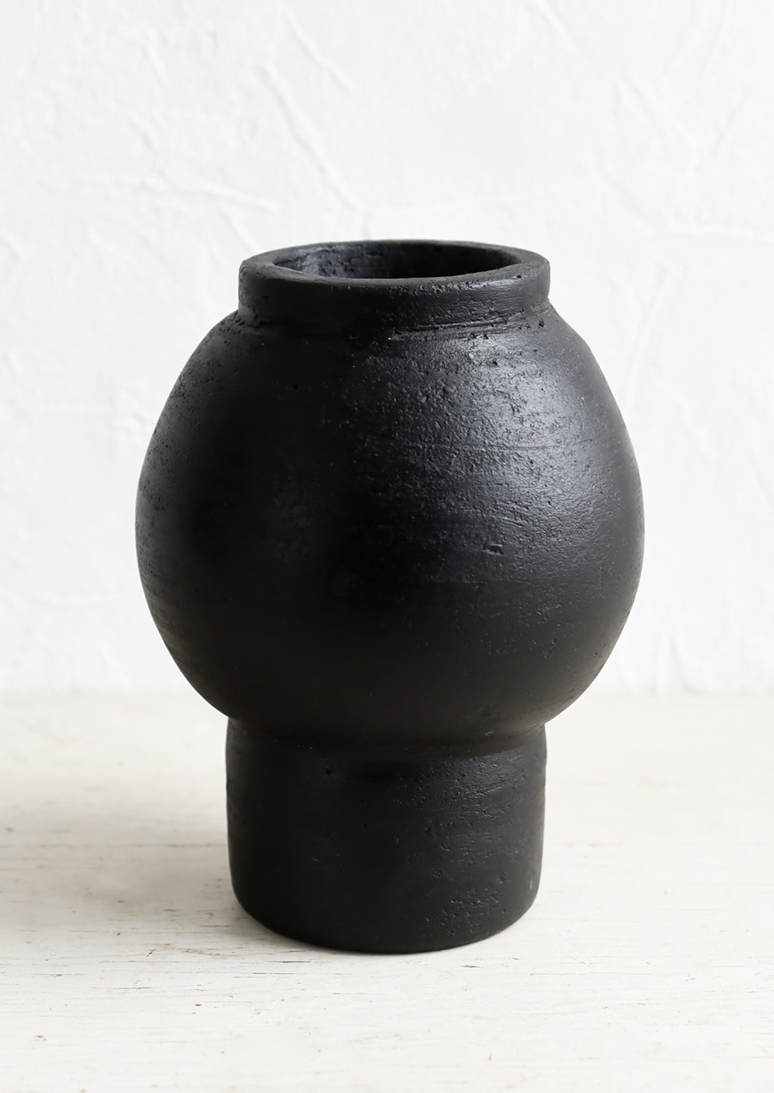 A vase in black terracotta clay with round shaped center and footed base.
