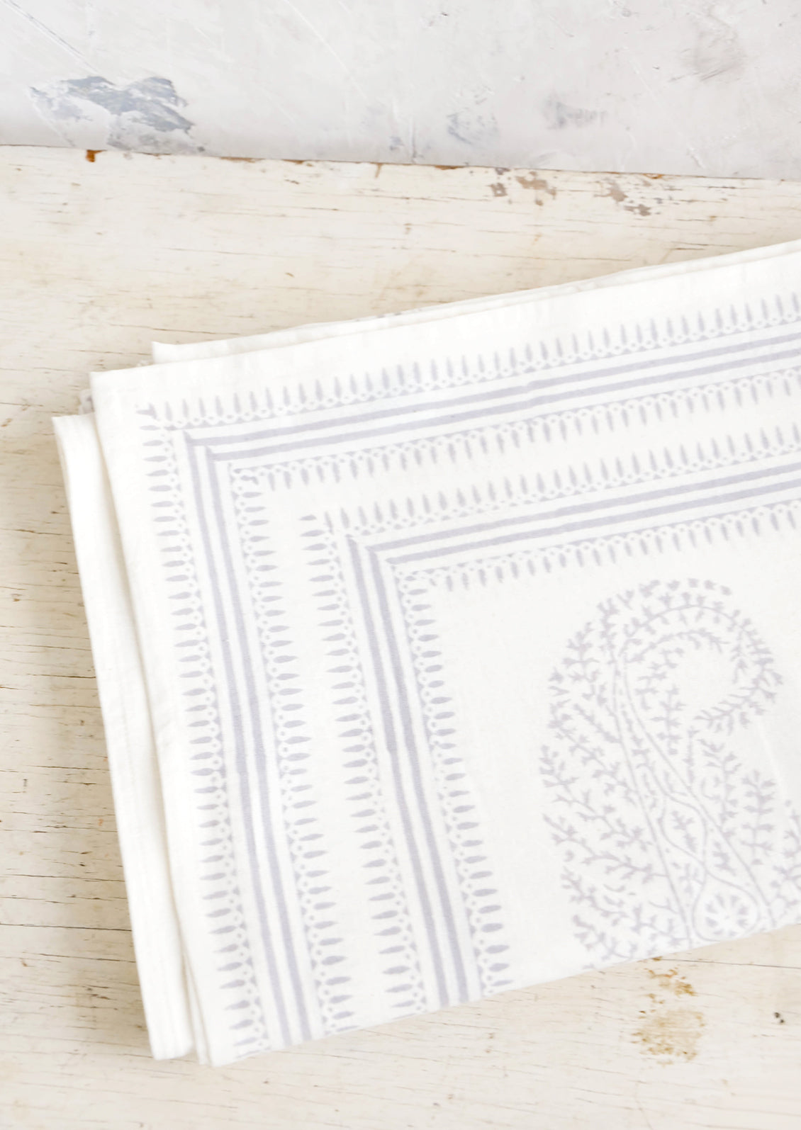 Folded white cotton tablecloth with grey paisley pattern