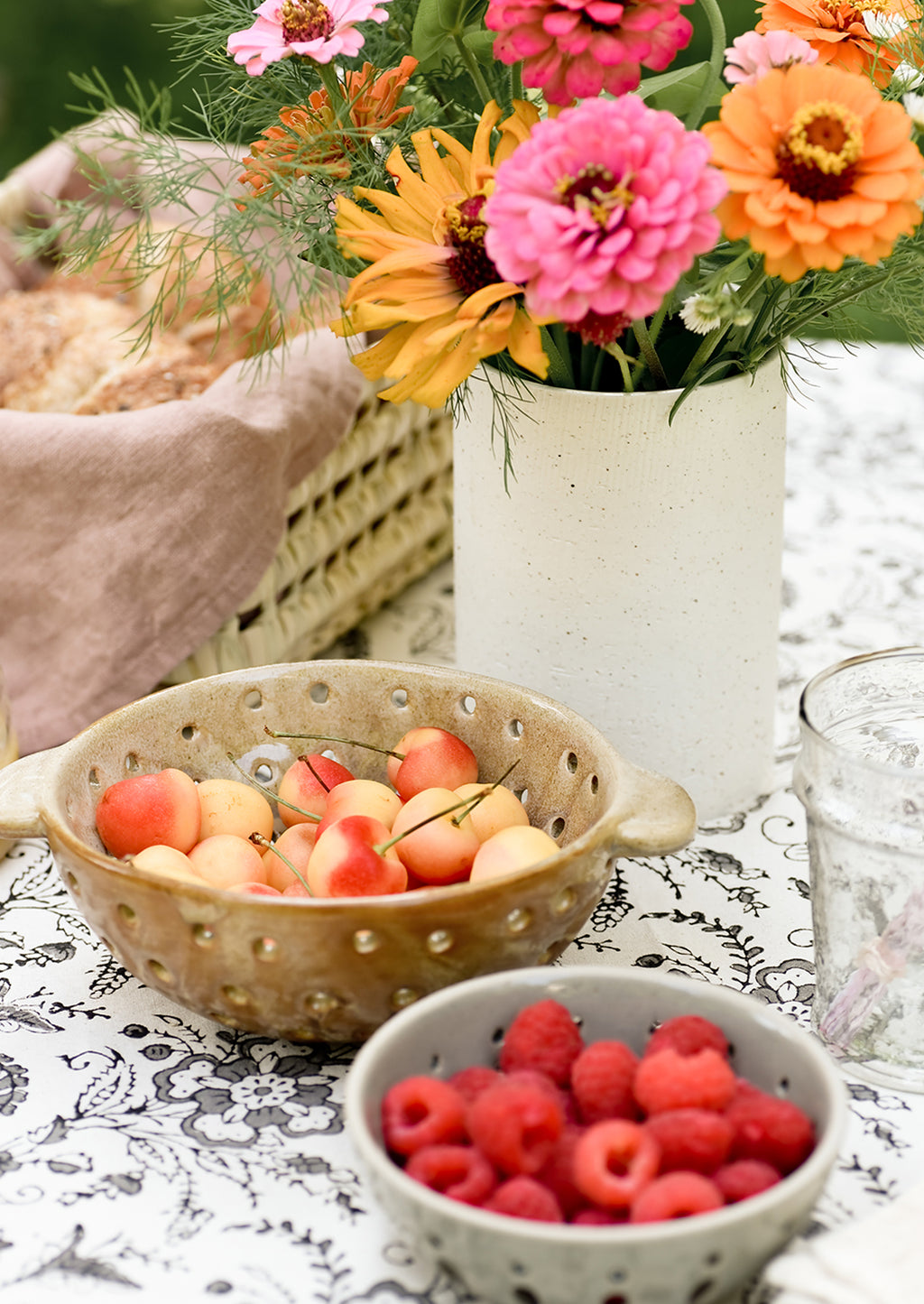 2: A vase with flowers on table with berry bowls.