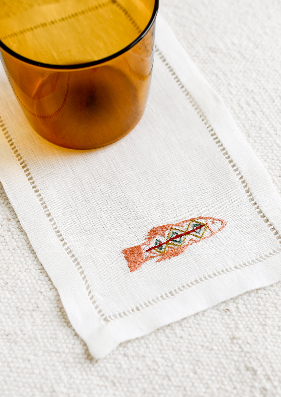 An white linen cocktail napkin with embroidered fish.