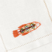 2: An white linen cocktail napkin with embroidered fish.