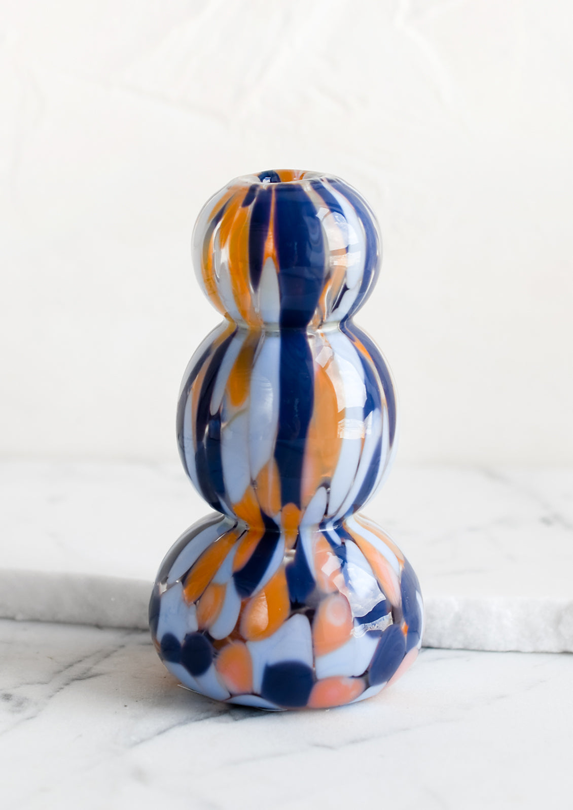 A bubble shaped bud vase in hand blown glass with blue and orange speckle pattern.