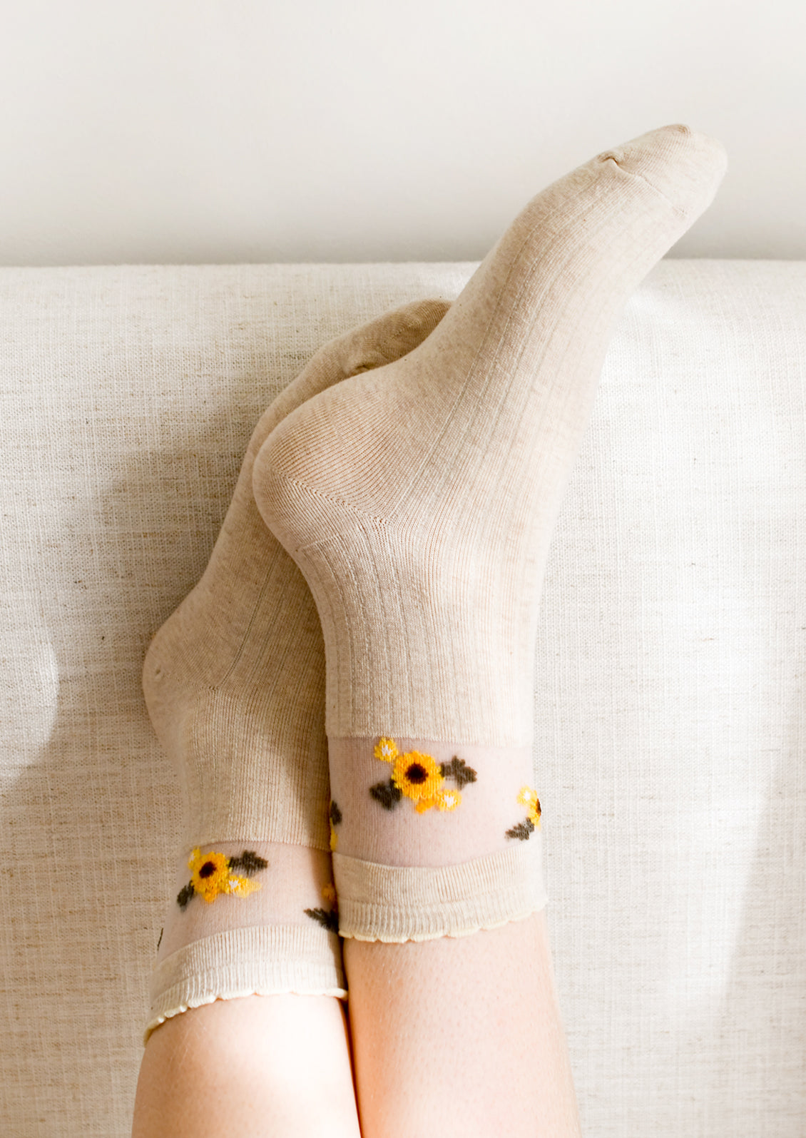 A pair of oatmeal colored socks with sheer mesh sunflower print band at ankle.
