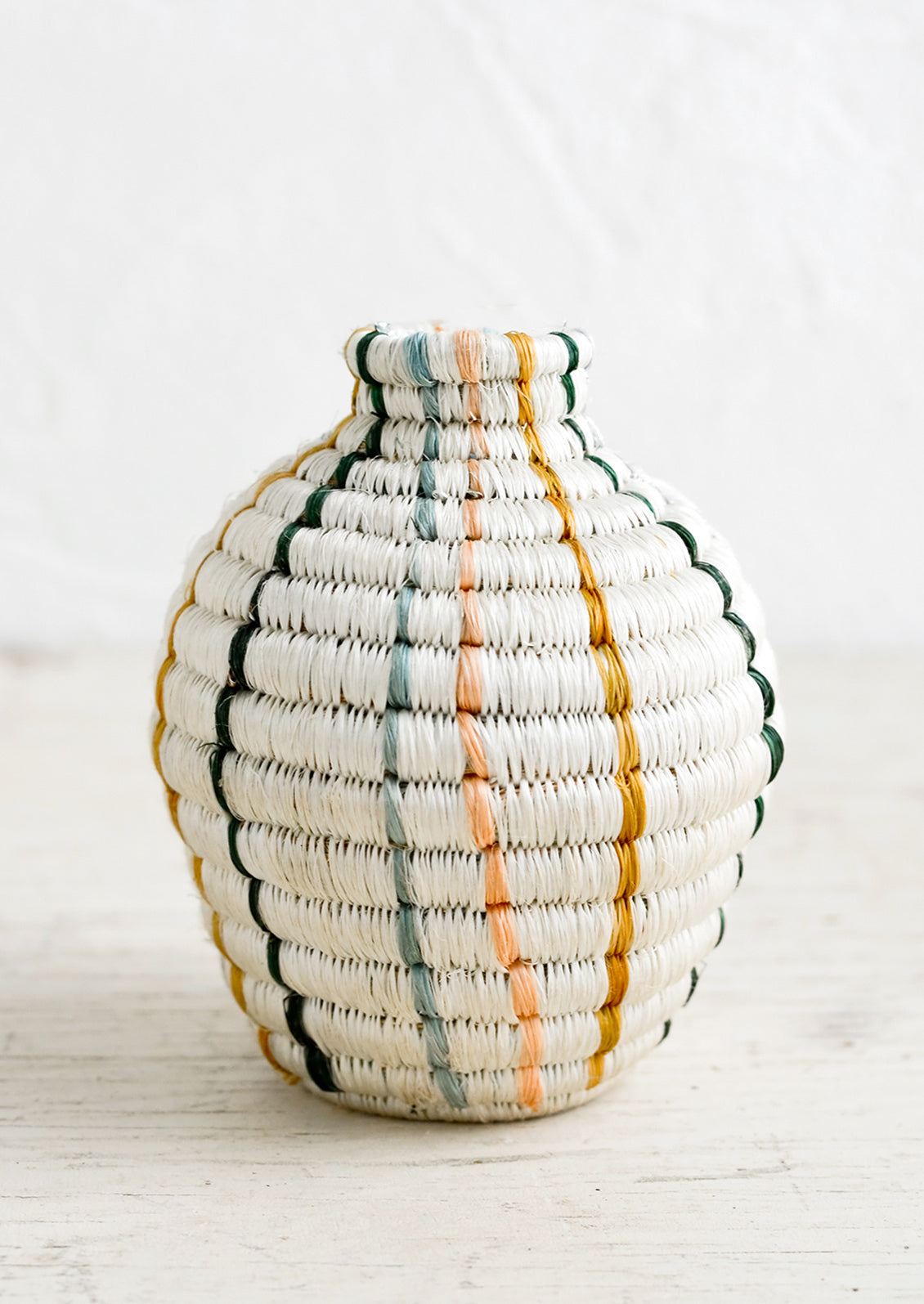 A decorative vase made from woven sweetgrass in white with vertical pastel stripes.