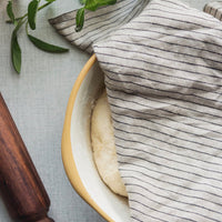 Natural / Black Pinstripe: A linen tea towel in tan and black pinstripe covering a bowl of rising dough.