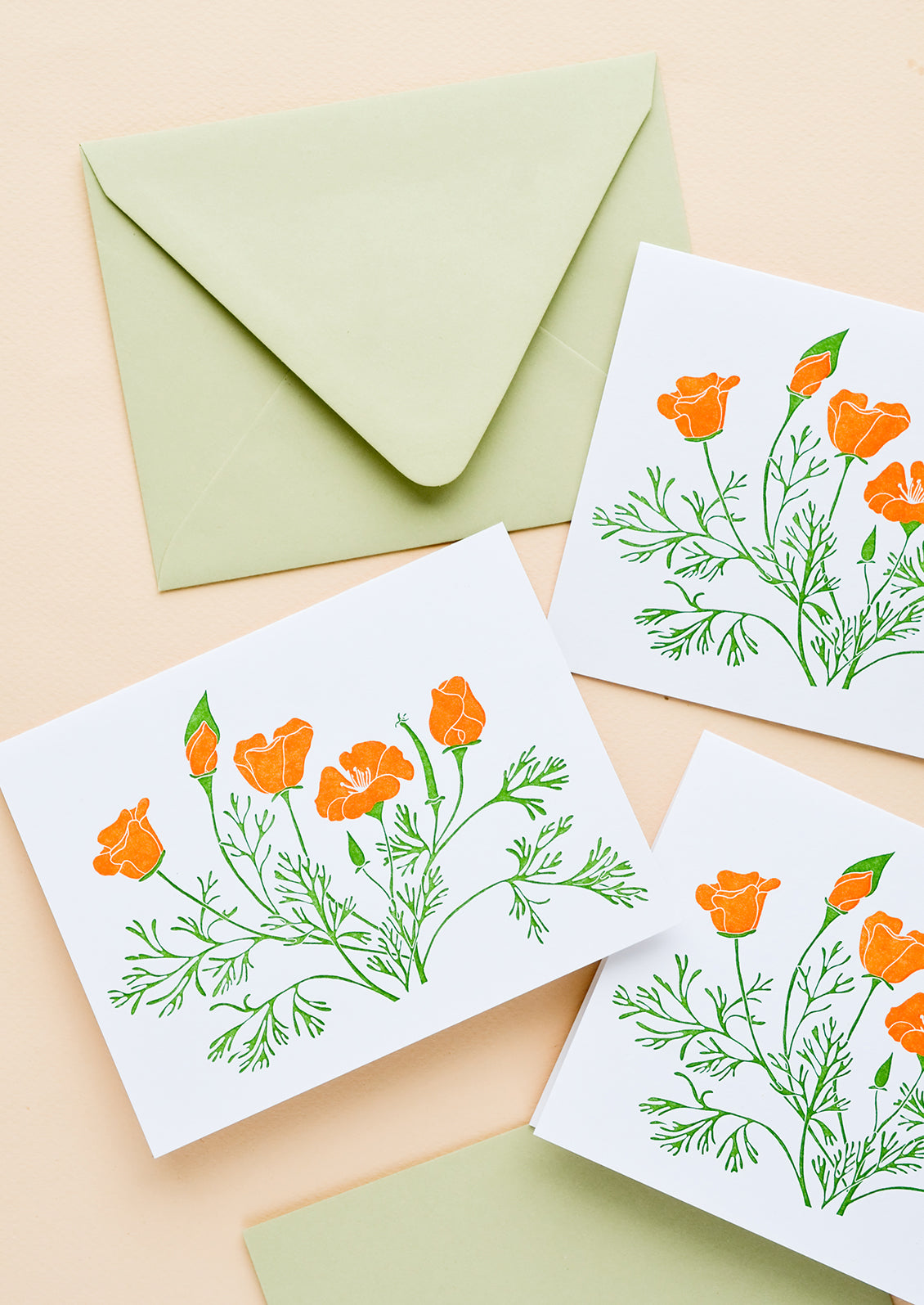 A set of white greeting cards with orange poppy flowers printed on front, paired with pastel green envelopes.