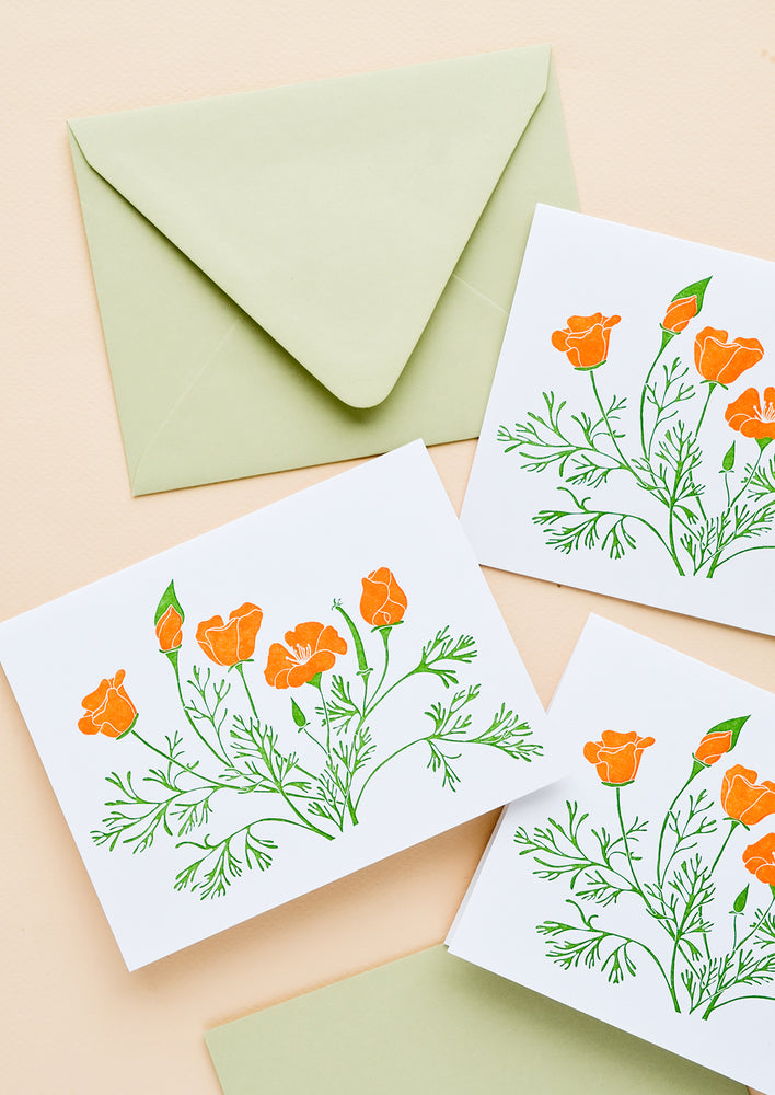 A set of white greeting cards with orange poppy flowers printed on front, paired with pastel green envelopes.
