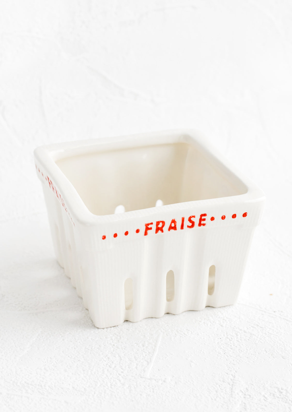 A white ceramic basket designed to look like a berry basket with "Fraise" printed in red lettering.