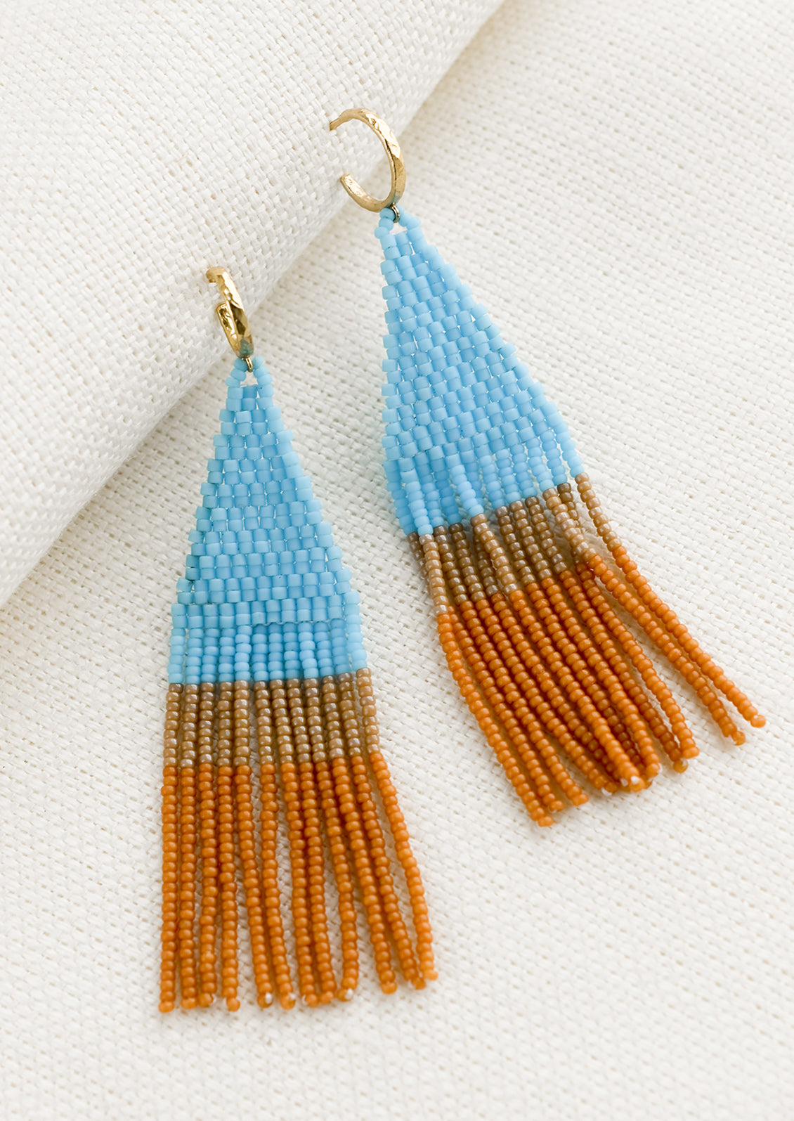 Beaded earrings featuring turquoise and brown beads layered into fringe, dangling from a gold hoop.