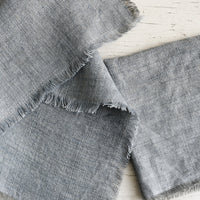 Smoke: Folded grey colored linen napkins with frayed edges.