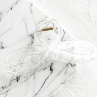 Clear: A curvy hair clip with knotted loop design in clear.