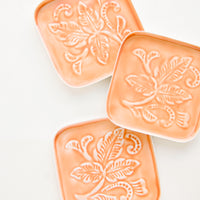 Peach: Square coasters in peach enamel with raised floral motif