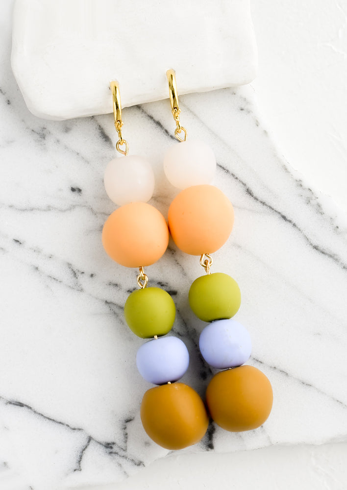 A pair of polymer clay drop earrings with colorful balls stacked together.
