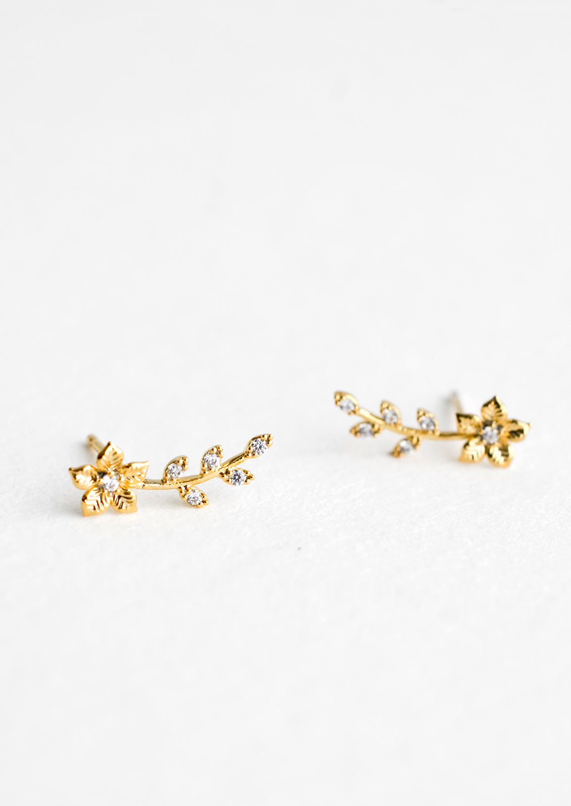 A pair of gold climber stud earrings with floral design decorated with crystals.