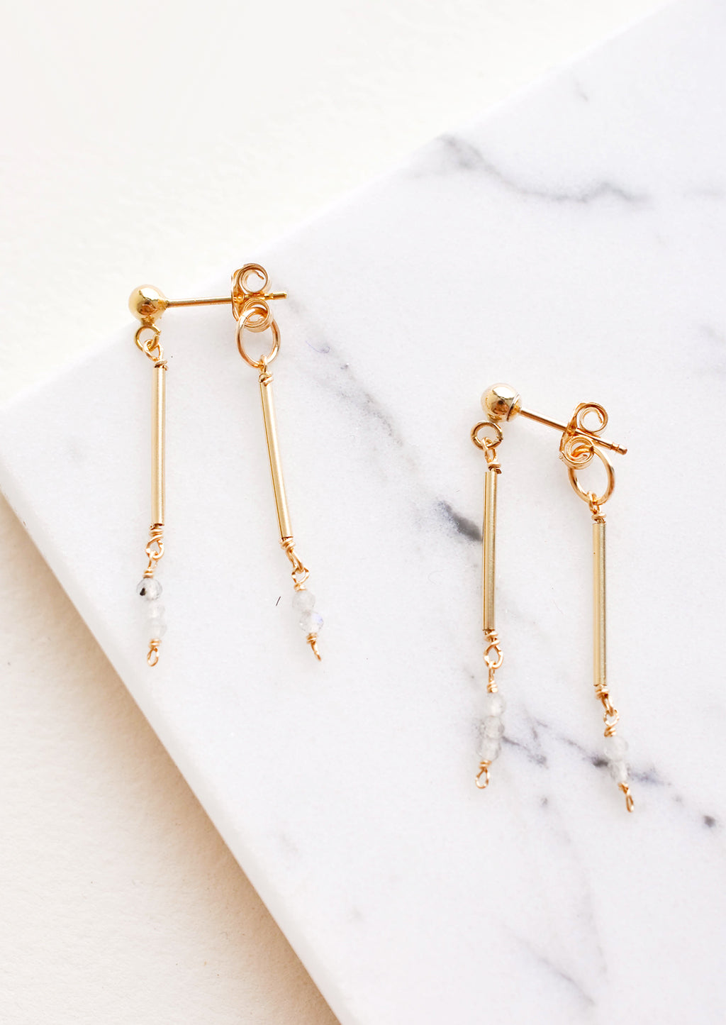 Moonstone: Two part dangling earrings featuring gold post and white beads hanging from each of the post and the earring back.