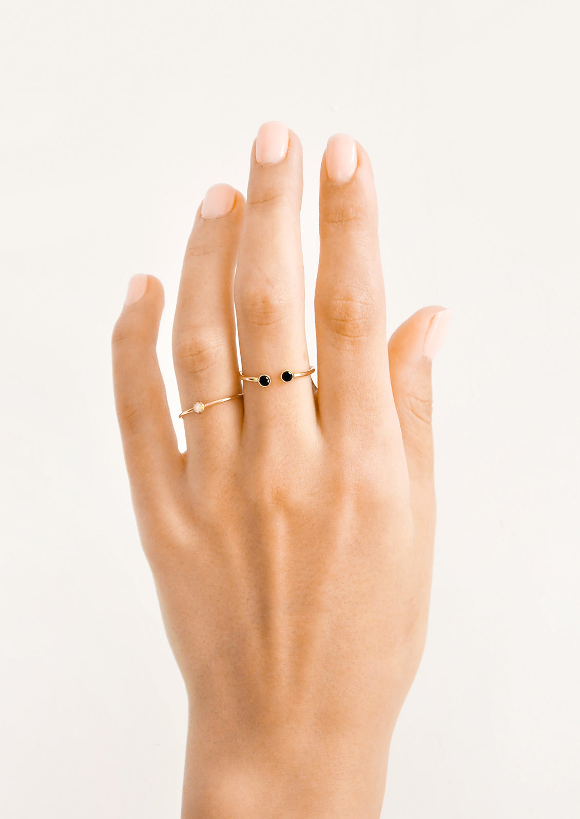Model shot showing hand wearing two gold rings with stones.