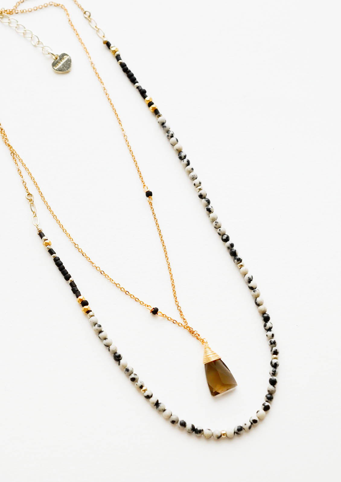 A two-layer gold necklace with one strand of small, round cream and black stones and another of the thin gold chain and brown gemstone pendant.