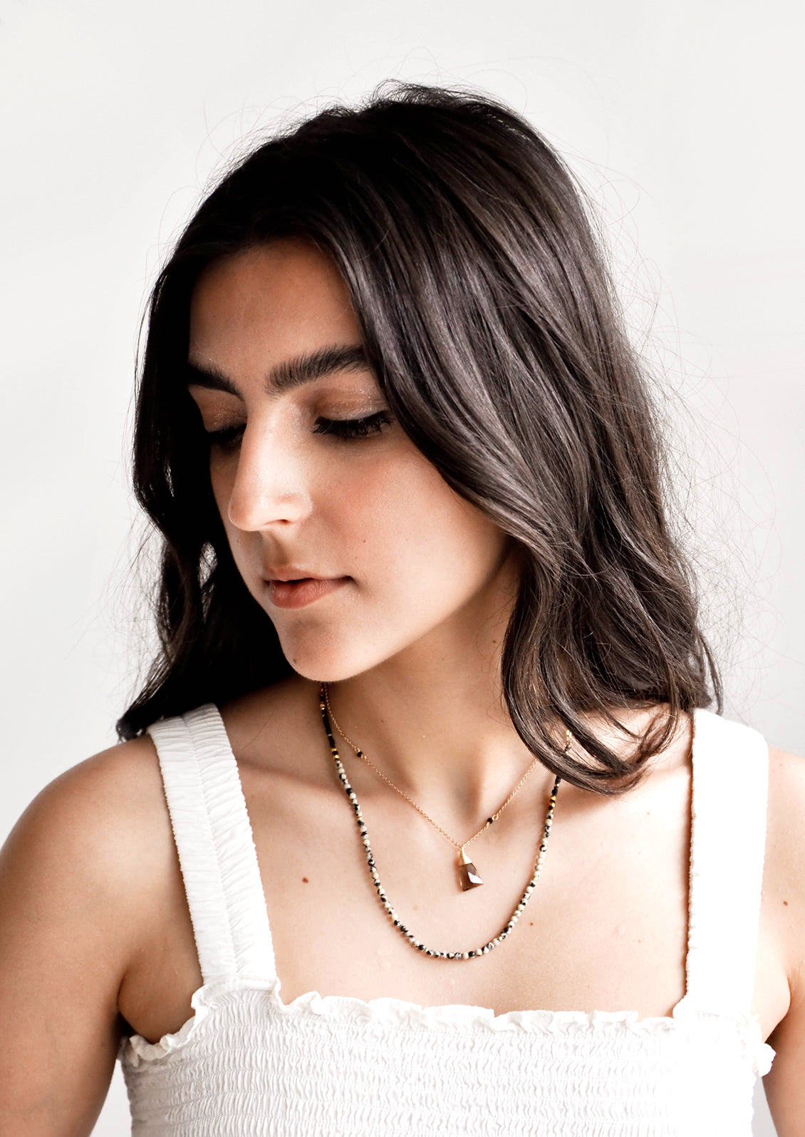 Model wears layered necklace and white tank top.