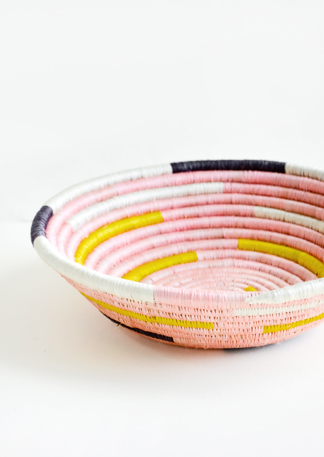 Round, shallow bowl made from woven sweetgrass in pink, white, yellow and black.