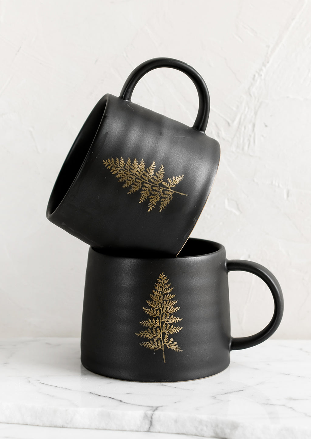 2: A black ceramic mug with single gold fern print.