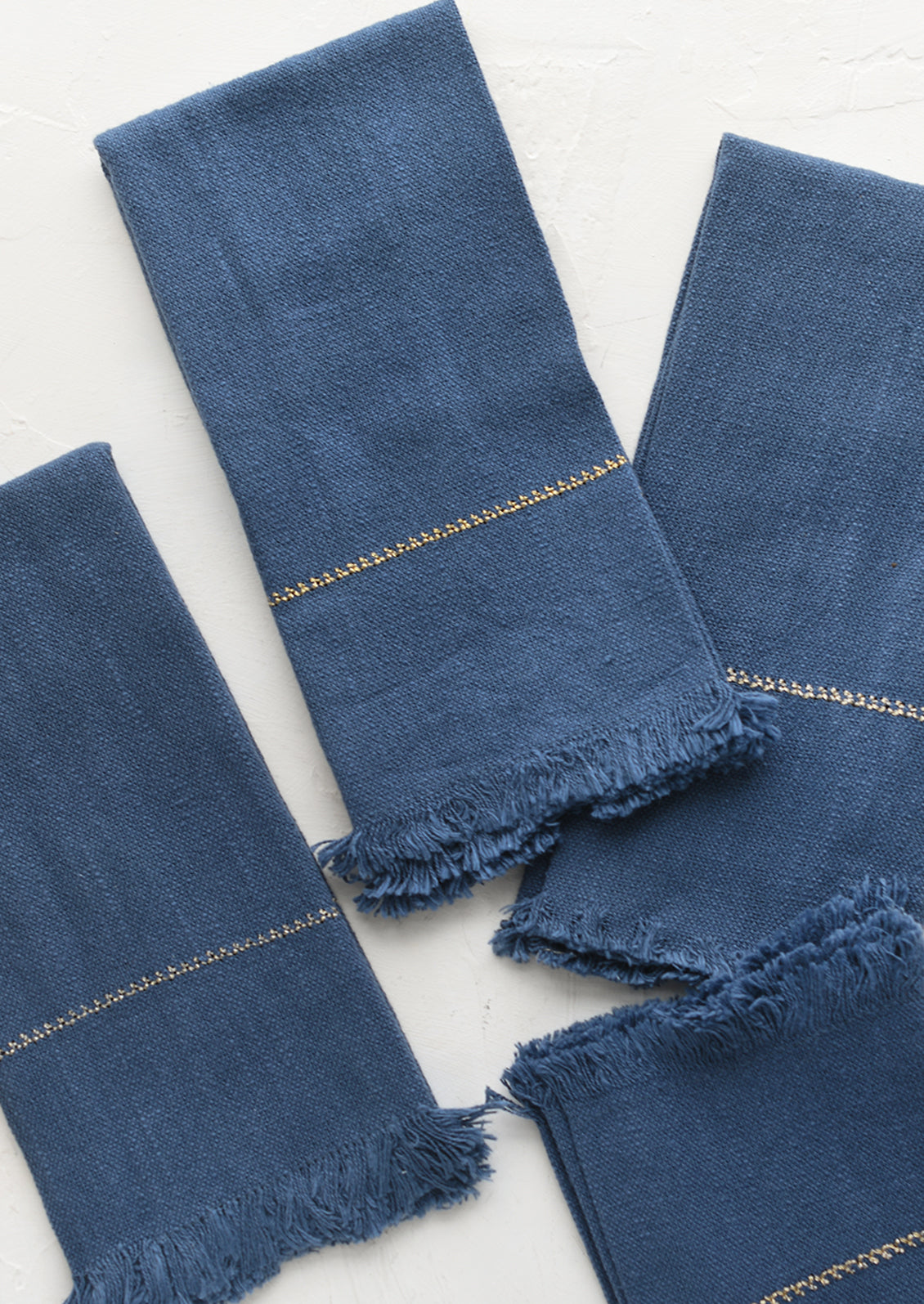 A set of four blue napkins with fine gold stitching.