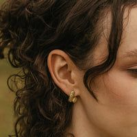 2: A woman wearing a pair of brass earrings.