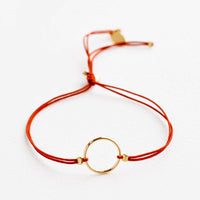 Rust: Bracelet with yellow gold circle charm centered on an adjustable red string.