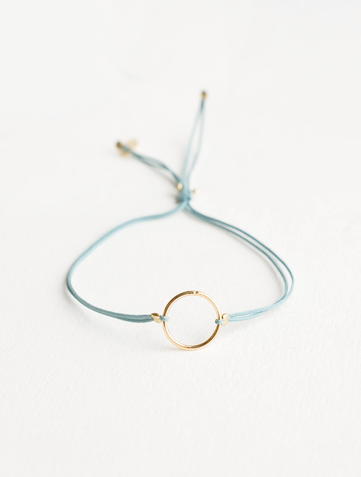 Bracelet with yellow gold circle charm centered on an adjustable teal string.
