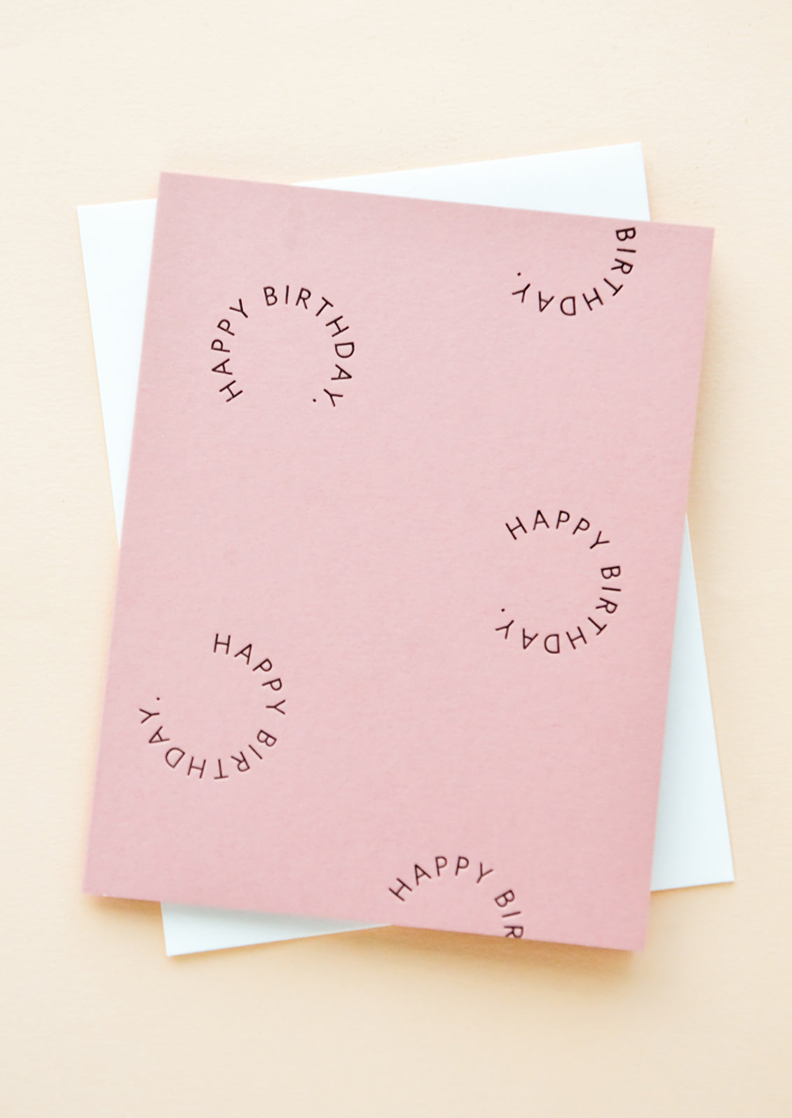 Pink notecard with the text "Happy birthday" set in a circle several times, with white envelope.