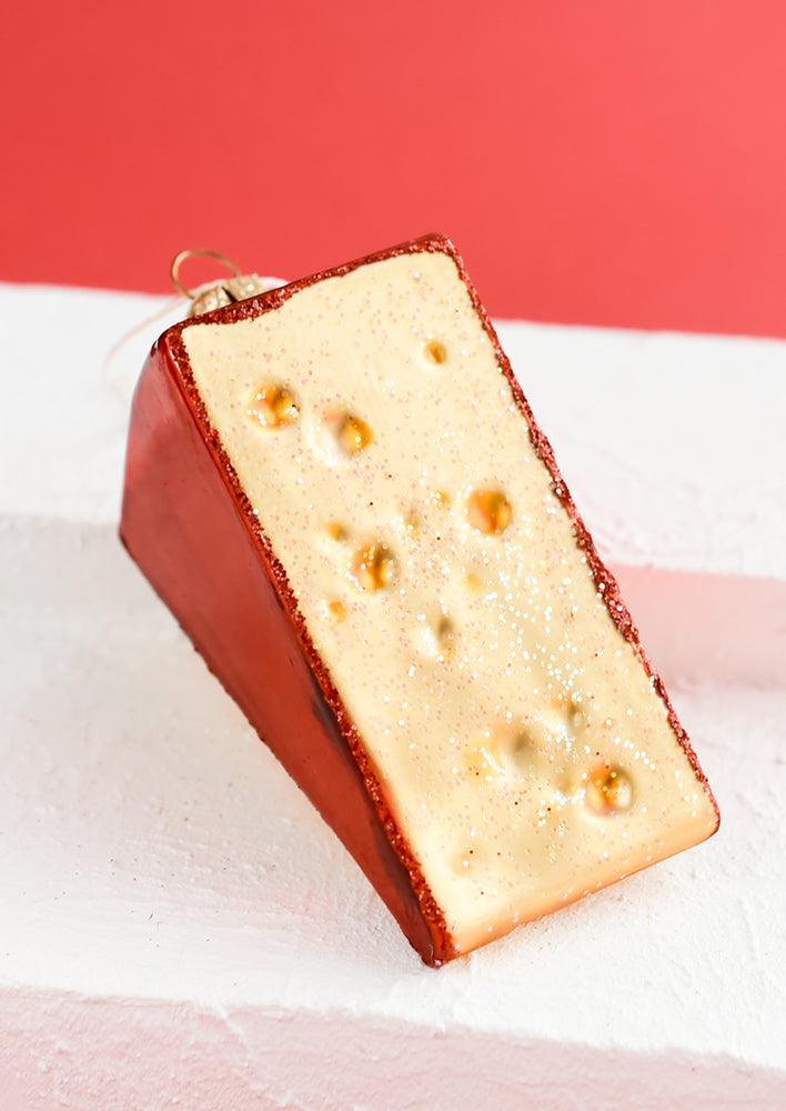 A glass ornament in the shape of cheese slice with red trim.