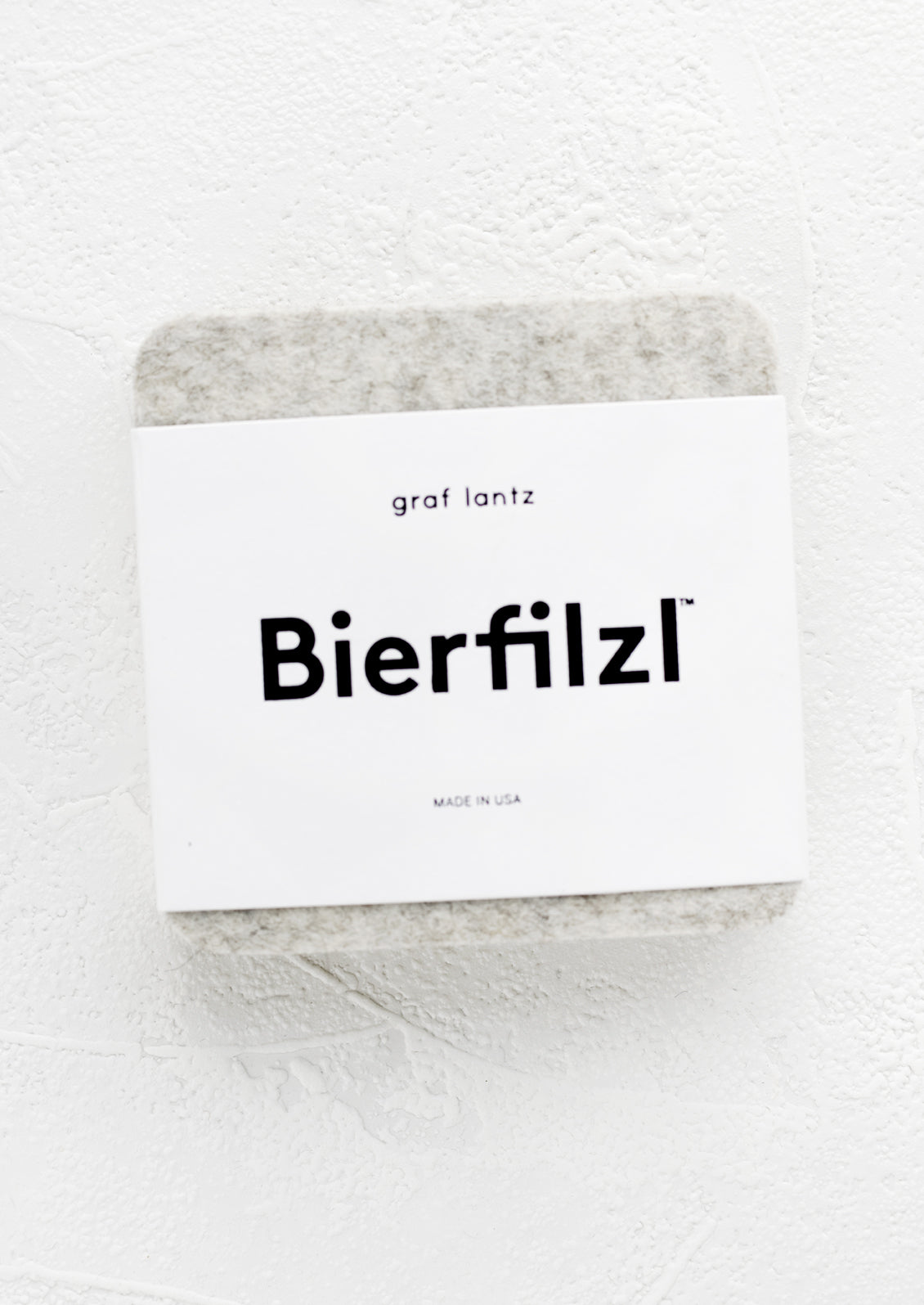 A package of square wool felt coasters in heathered white.