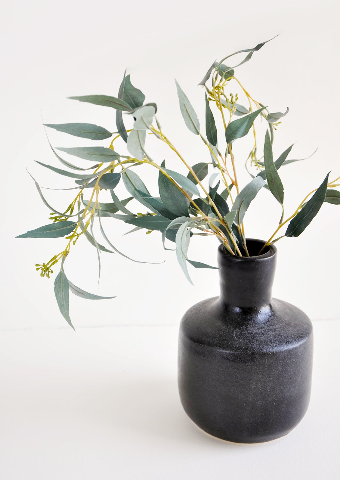Glossy black ceramic vase with wide base and narrow opening, displayed with eucalyptus branch