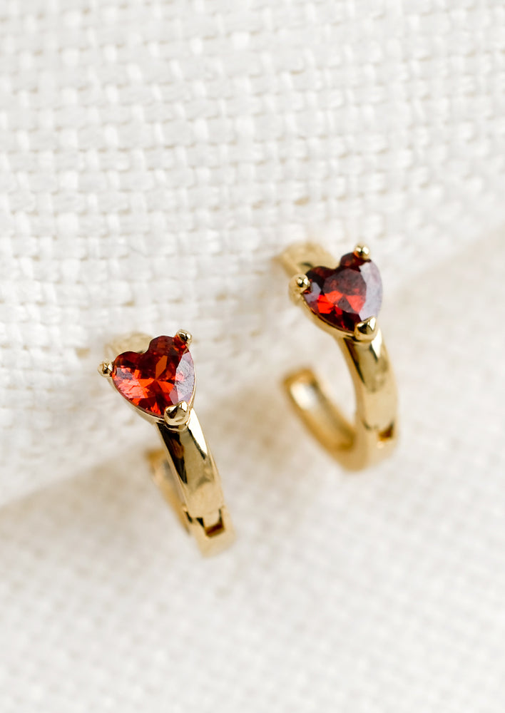 A pair of small gold hoop earrings with red crystal heart detail.