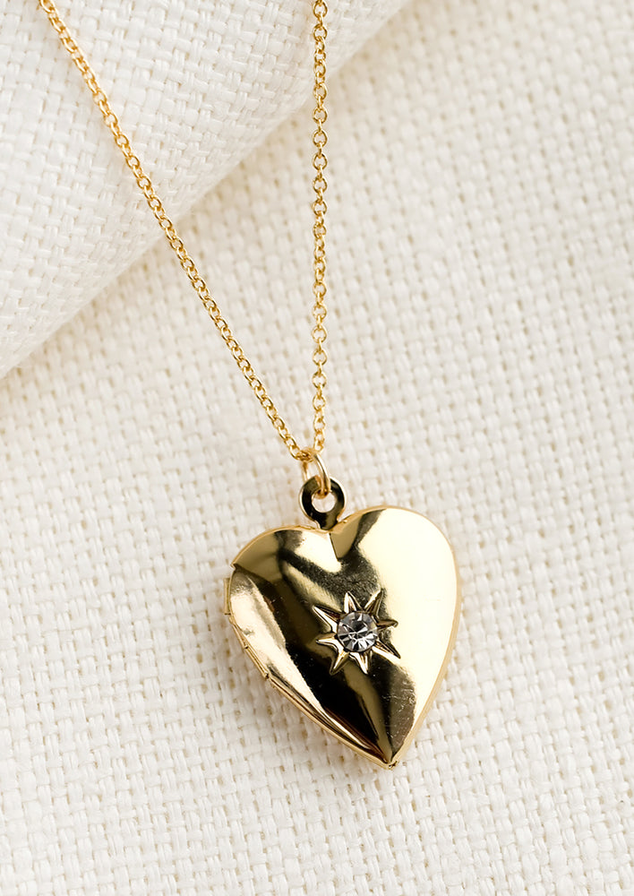 1: A gold locket necklace in heart shape with single crystal at center.