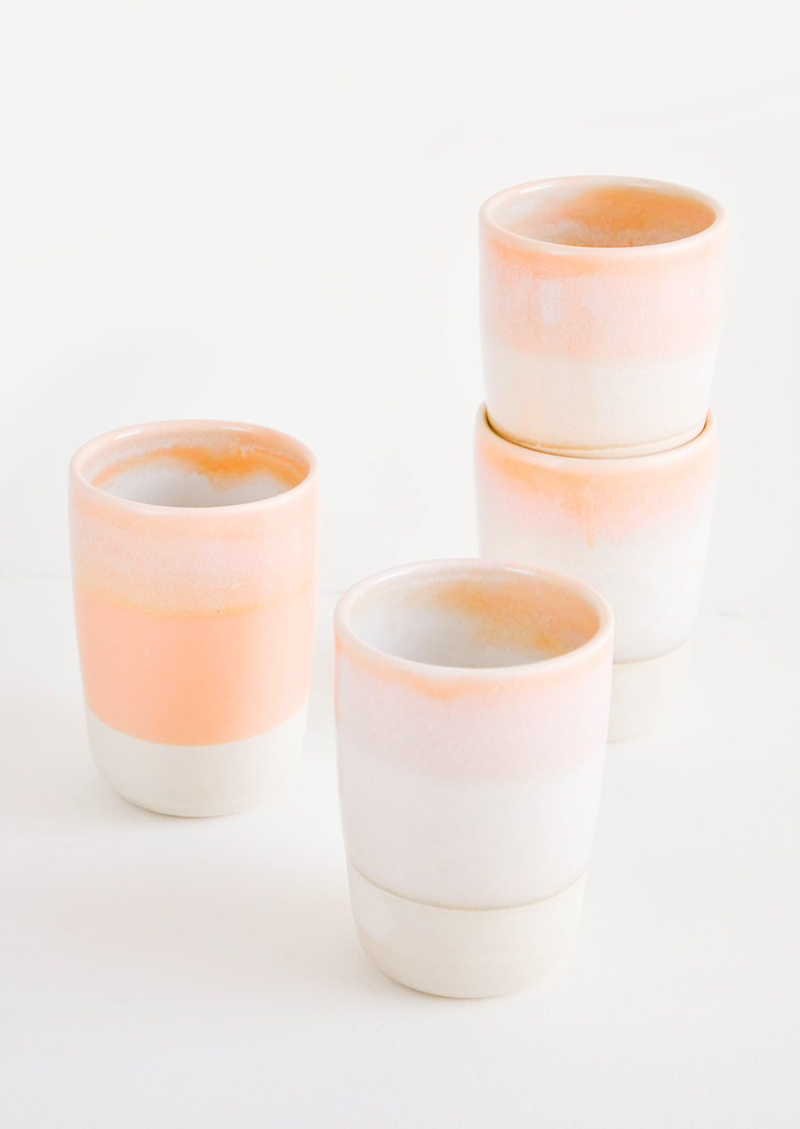 Four ceramic tumblers with unfinished bottoms and orange glaze.