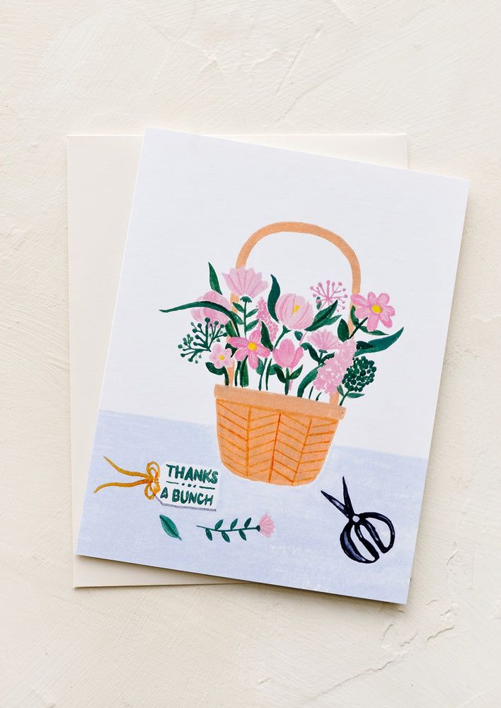 A greeting card with flowers arranged in a basket, small text reads "Thanks a bunch".