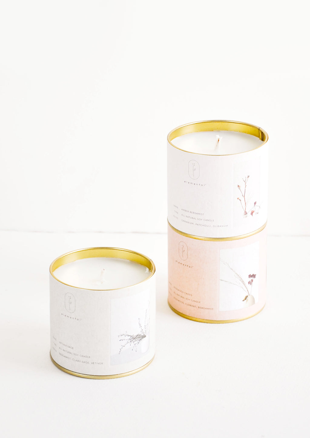 1: Three candles in brass tins with paper labels of gray, beige, and pale pink.