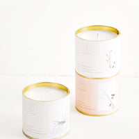 1: Three candles in brass tins with paper labels of gray, beige, and pale pink.