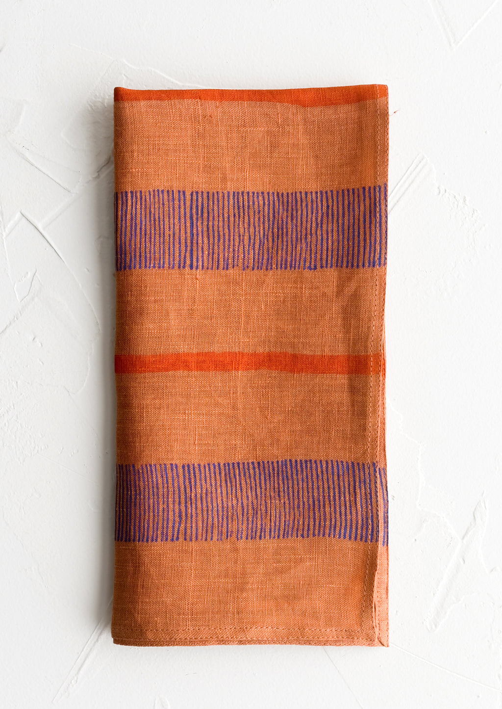 1: A terracotta linen napkin with block printed stripe design.